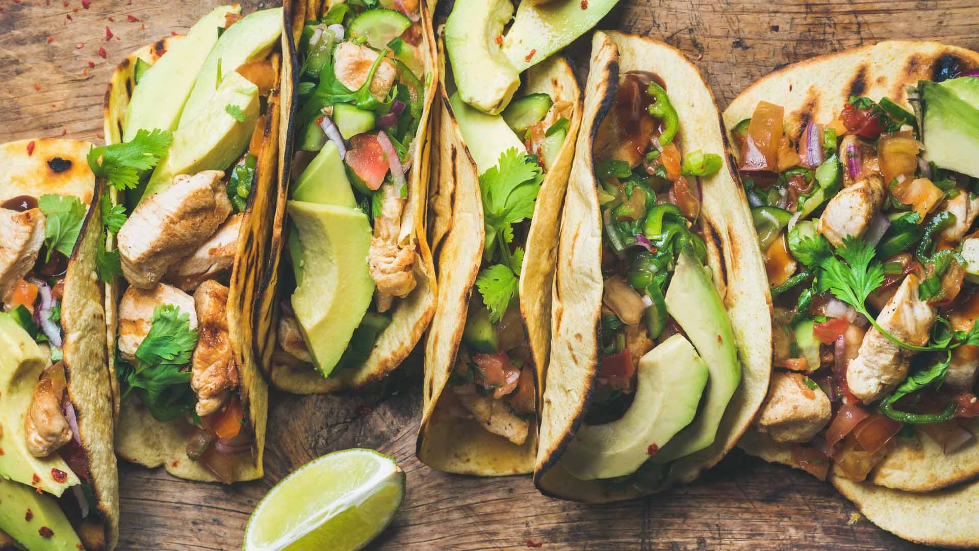 Tacos with grilled chicken, avocado, fresh salsa sauce and limes over rustic wooden background, top view. Healthy low carb and low fat lunch or food for company. Dieting and weight loss concept