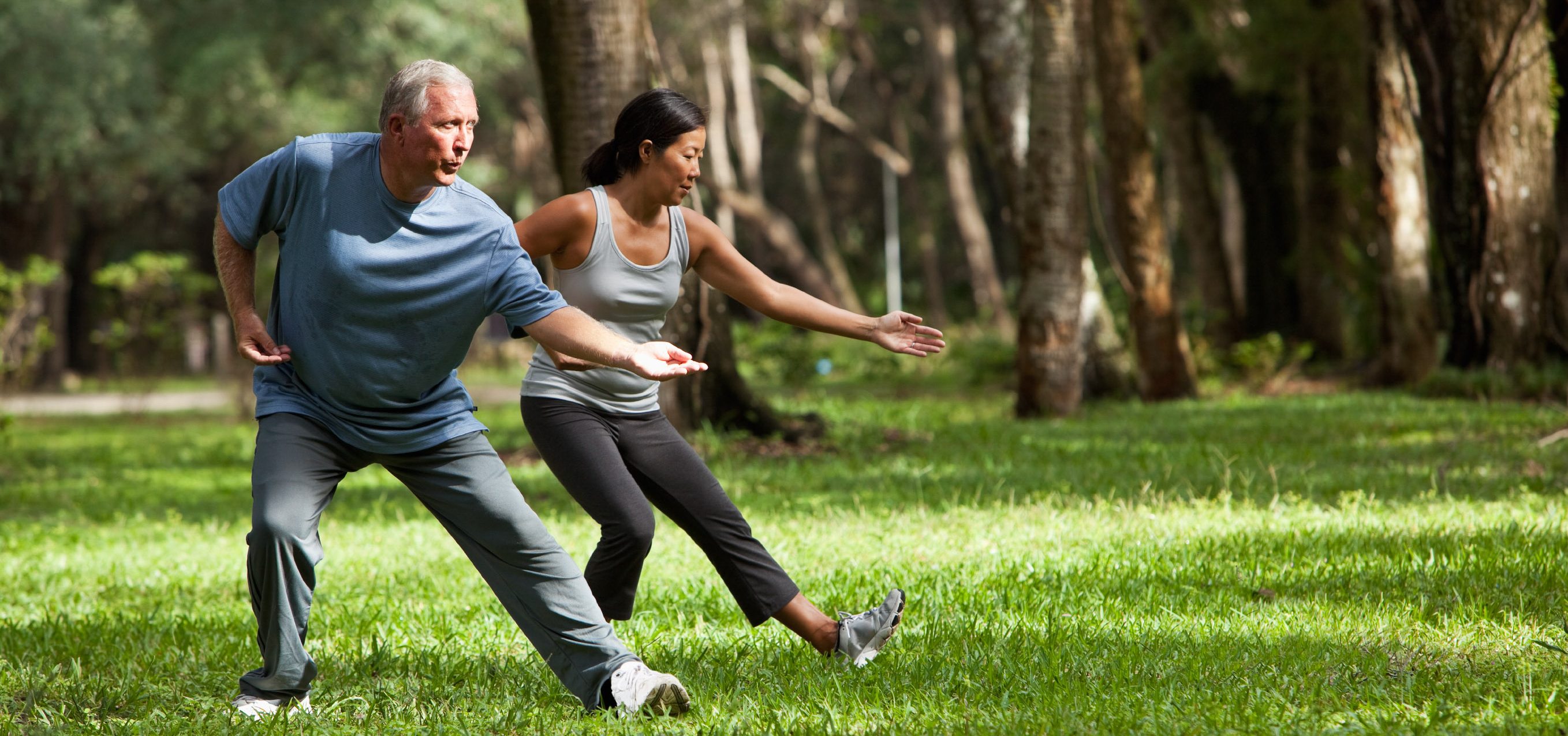 Tai chi class - senior man (60s) and mature Asian woman (40s) practicing tai chi in park.