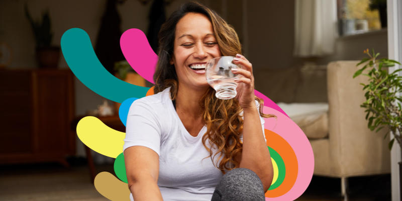 Woman sititng outside laughing while holding a glass of water