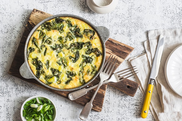 Potato and spinach tortilla in a pan on a light background. Delicious appetizer or snack, top view