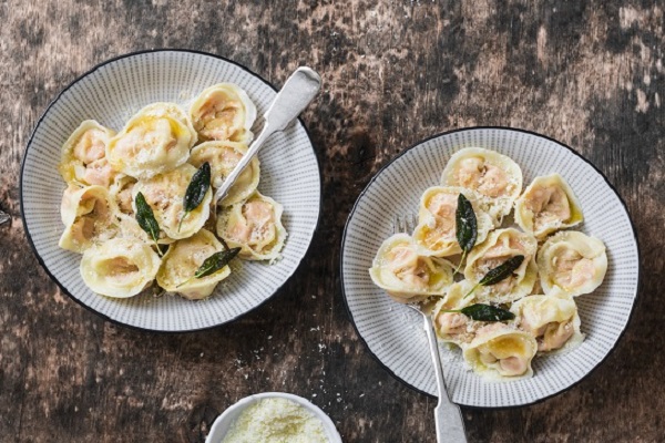 Pumpkin ravioli with sage butter and parmesan cheese on wooden background, top view. Delicious vegetarian, seasonal comfort food