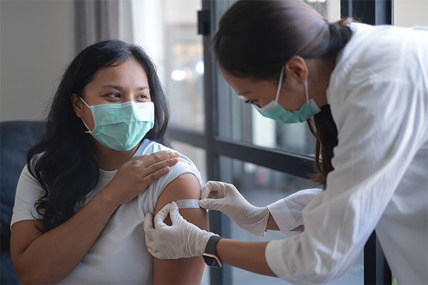 woman with mask getting bandaid applied after vaccination