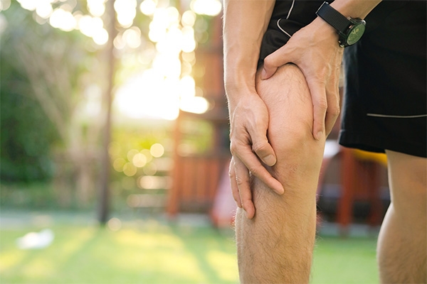 man outdoors holding knee with his hands