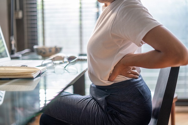 Woman in home office suffering from back pain sitting at computer desk