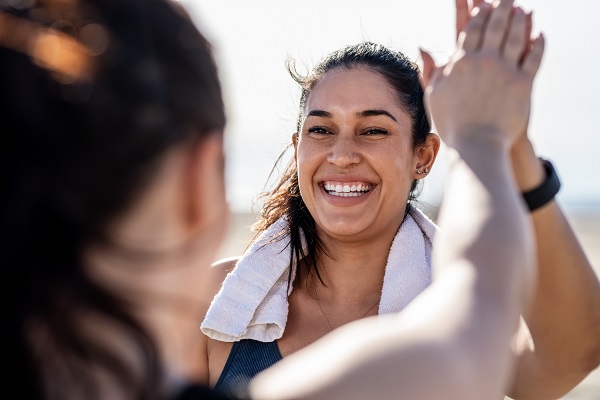 Smiling woman giving high five to her friend after exercising. Woman looking happy after a successful workout session outdoors.