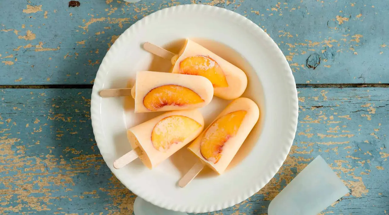 Homemade peach popsicles on a plate, set against a rustic blue wooden surface, giving a summertime vibe.