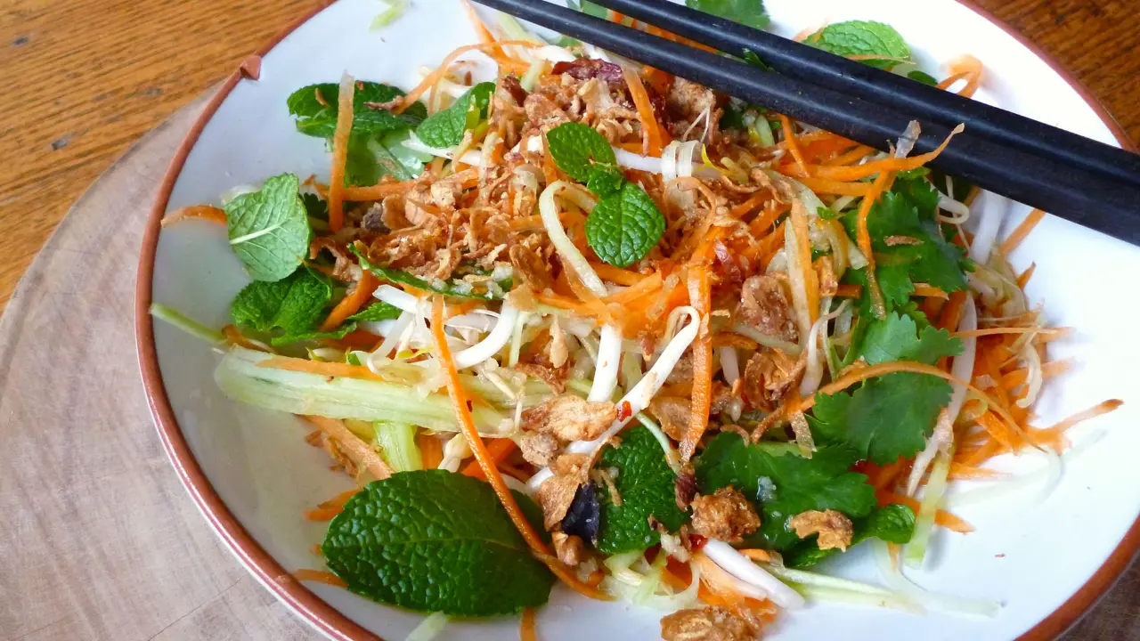 A vibrant Vietnamese salad with shredded carrots, bean sprouts, fried onions, and herbs in a white bowl with chopsticks, ready to be enjoyed.
