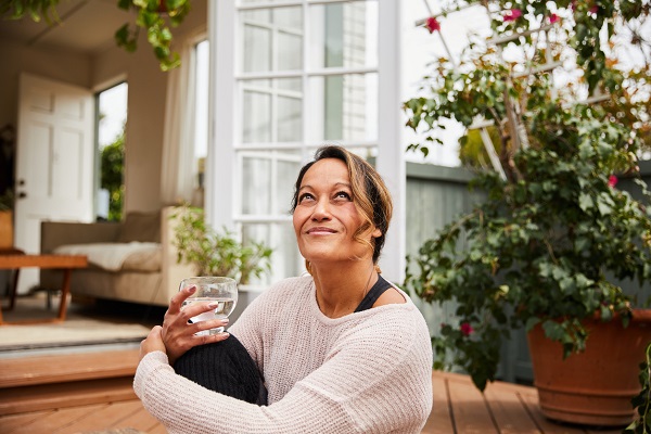Mature woman smiling while sitting alone on her patio outside drinking a glass of water