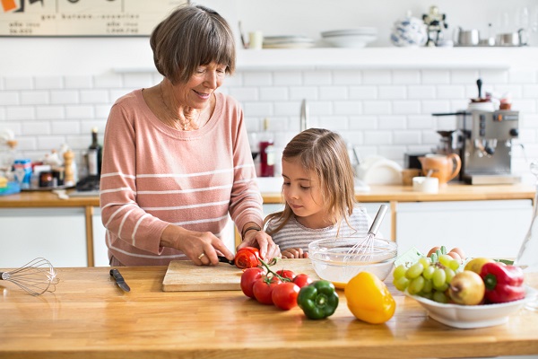 Portrait of a senior woman and little girl chopping vegetables in the kitchen at home