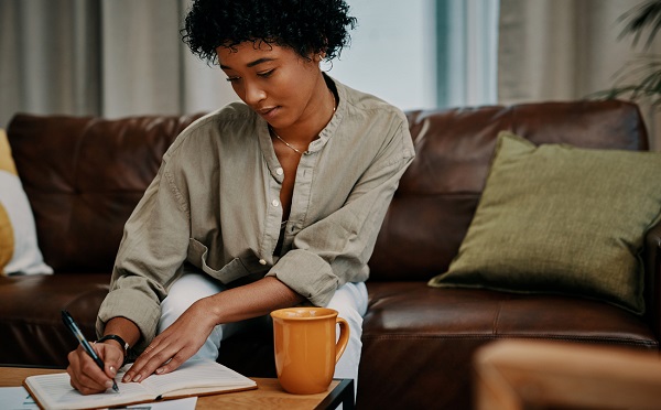 Cropped shot of a beautiful young woman writing in her notebook while sitting at home