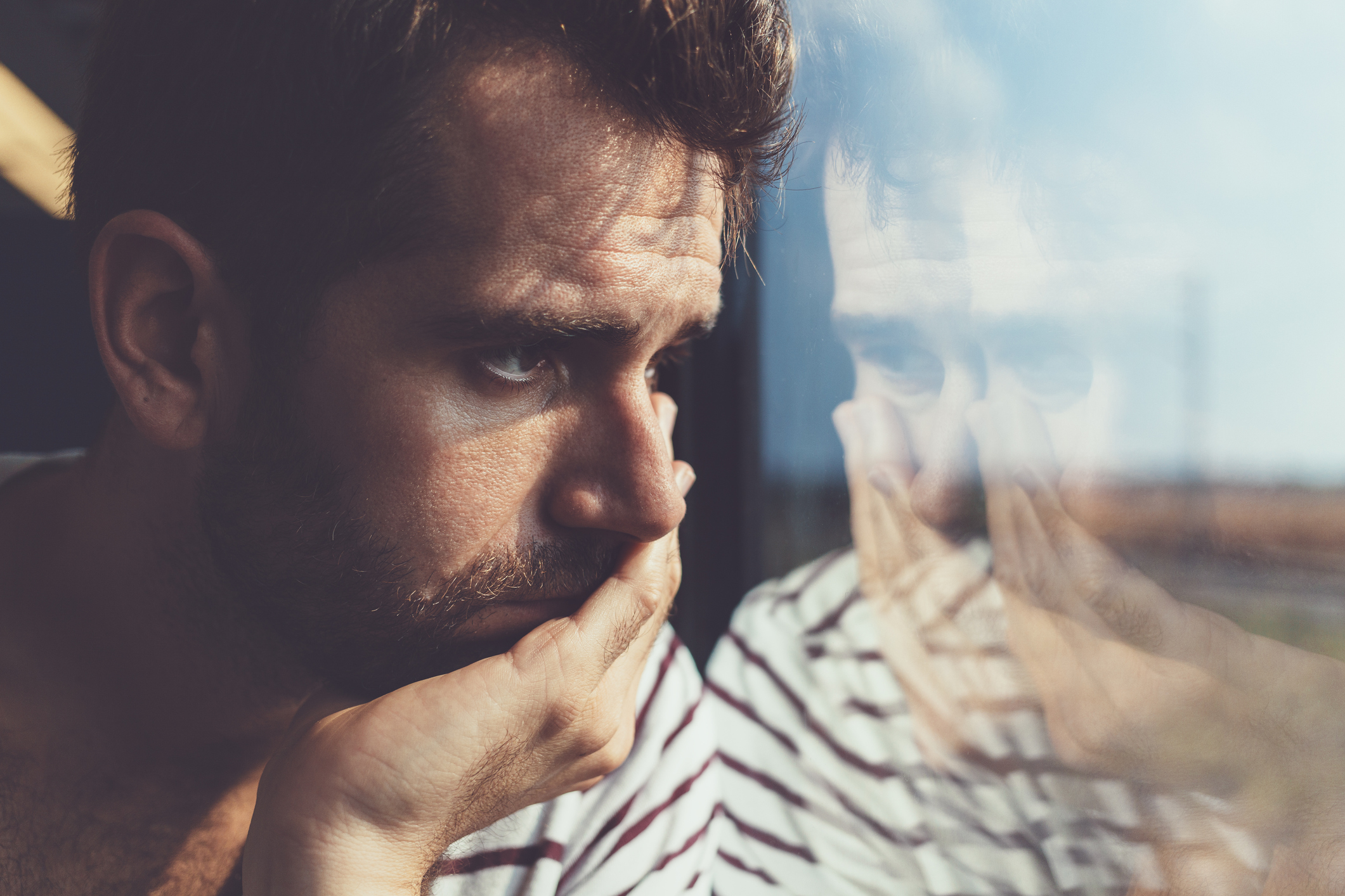 606671220 Sad young man looking through the window