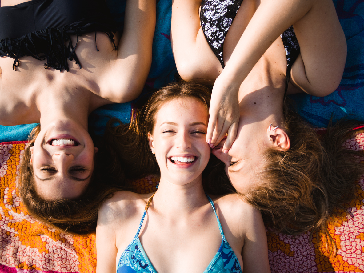 Three girls having fun lying on a towel on the beach at summer