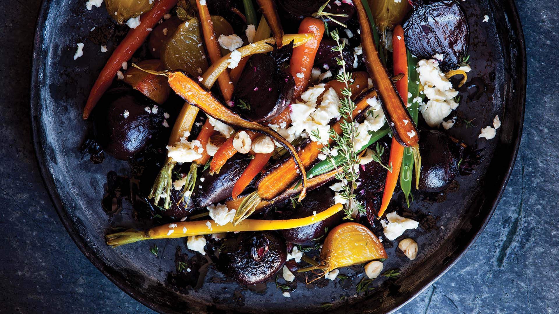 Close up of yellow and red beetroot, colourful carrots and beans roasted with a delicious topping of crumbed cheese, roasted hazelnuts and thyme sprigs