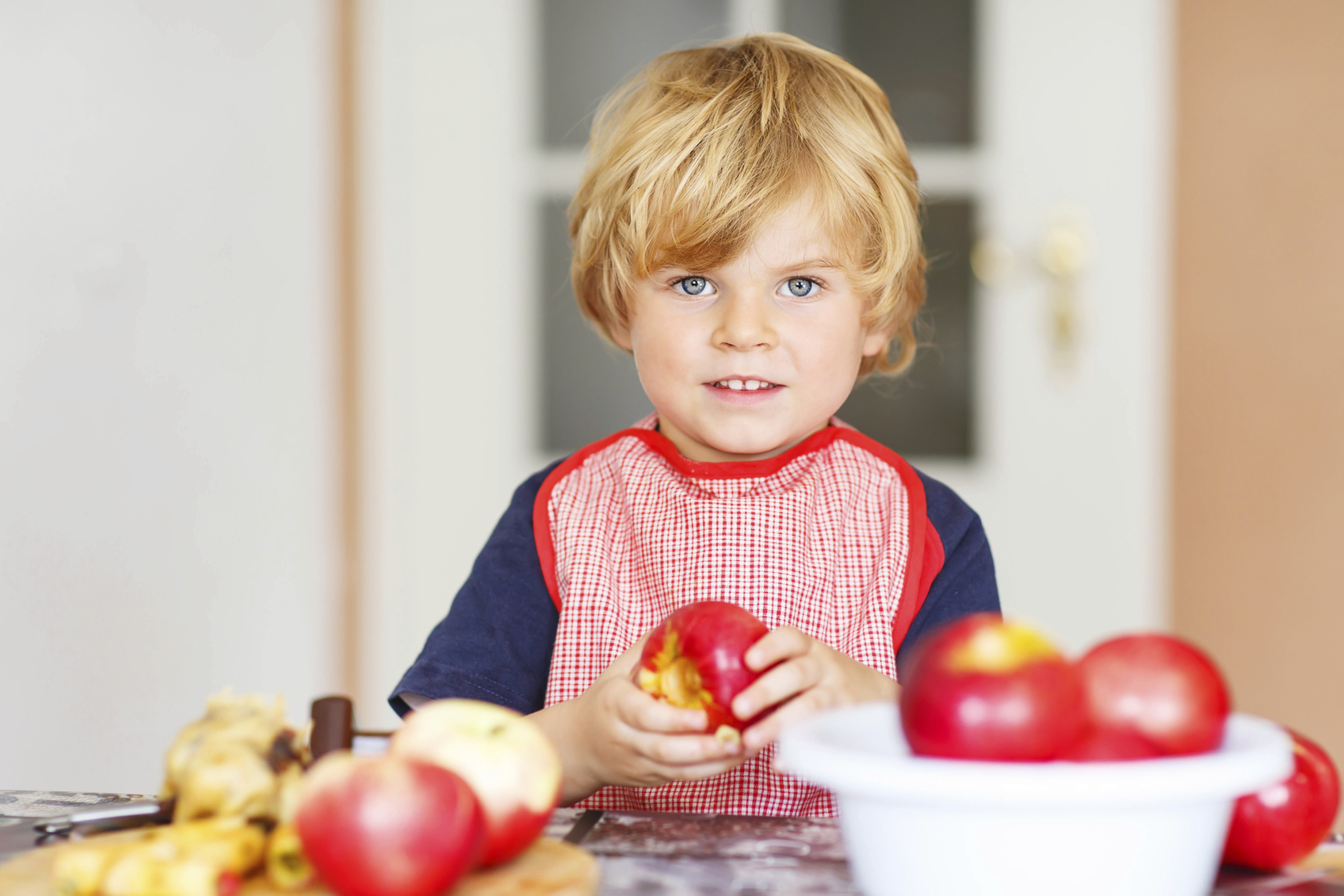 Funny cute kid boy helping and baking apple pie in domestic kitchen, indoor. Child filling apples with marzipan