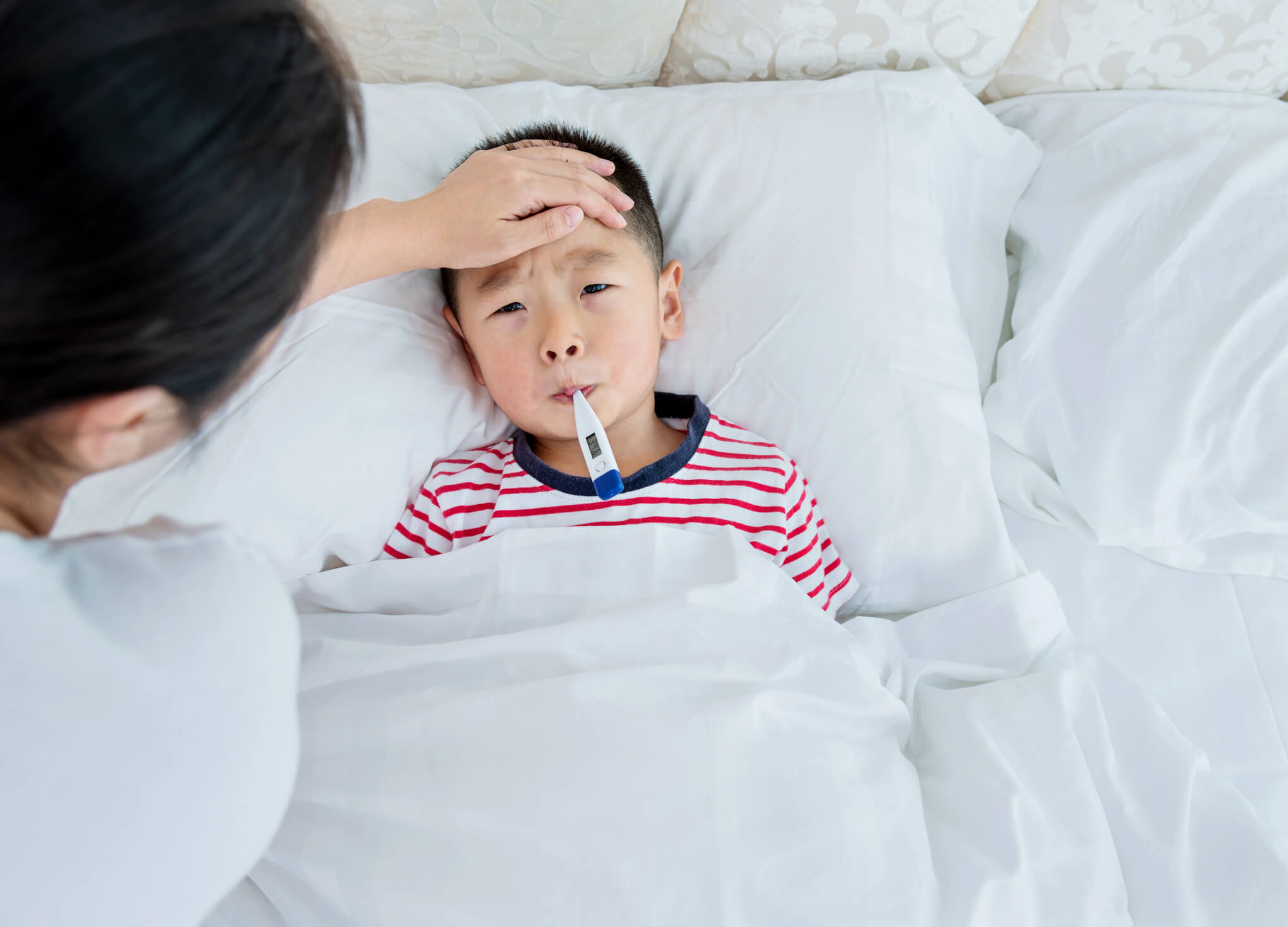 A sick child in bed with a thermometer in his mouth