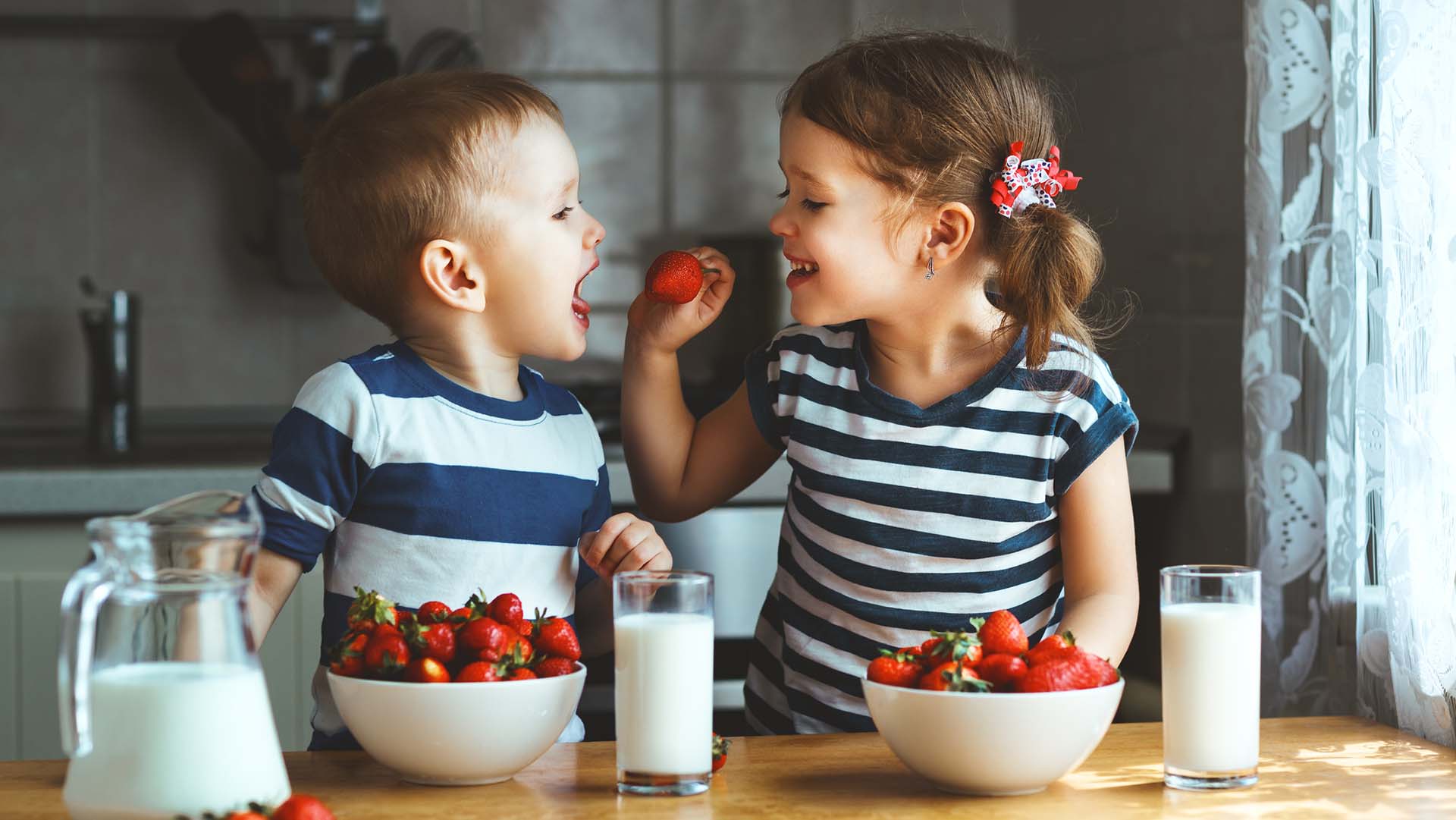 Happy children girl and boy brother and sister eating strawberries with milk