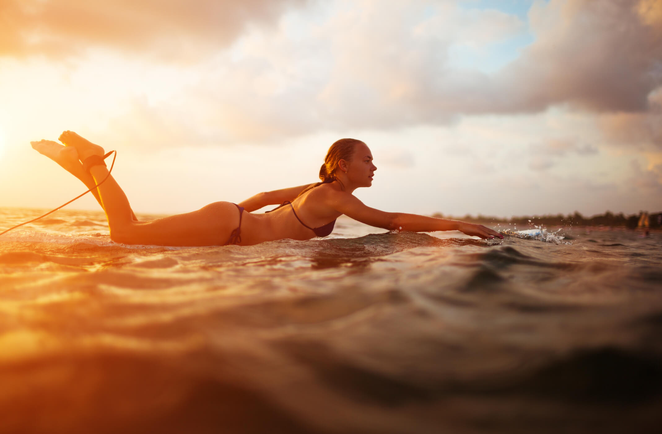 surfer girl paddling in ocean on white surfboard