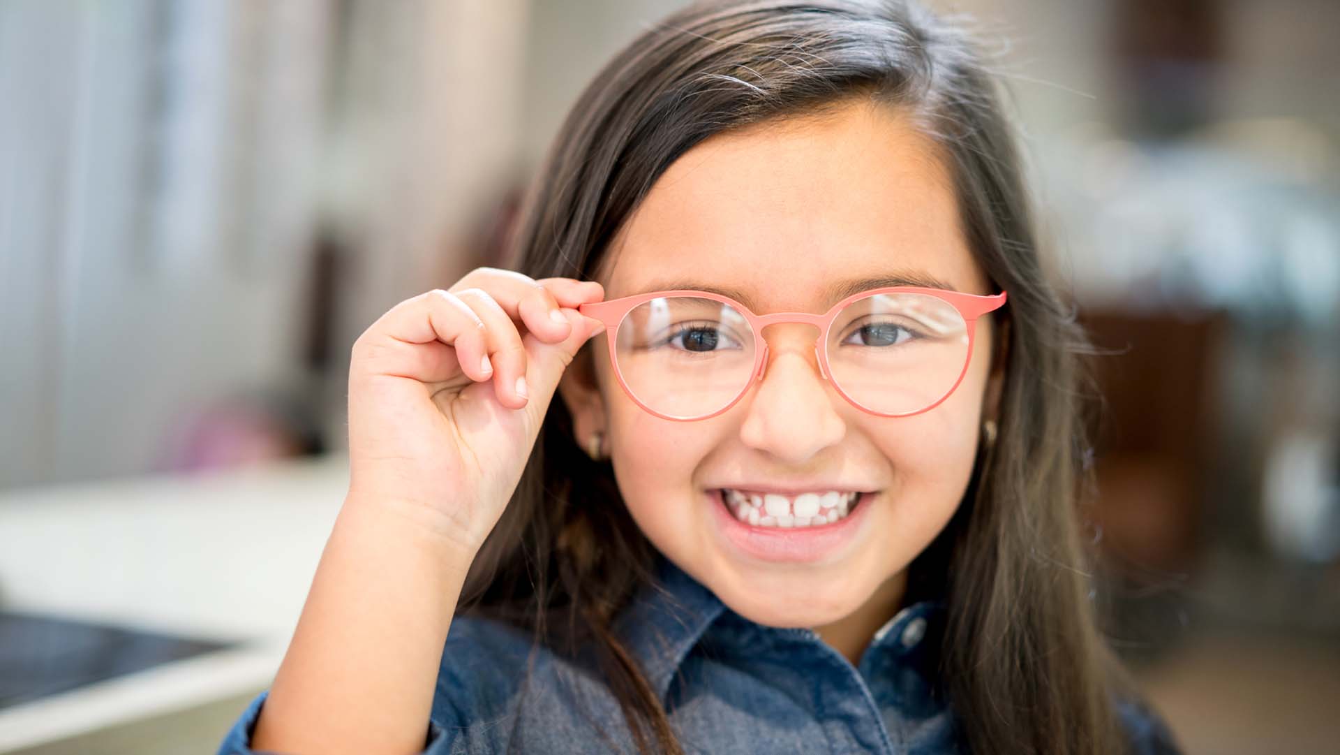 Little girl trying glasses at the optician - healthcare and medicine concepts