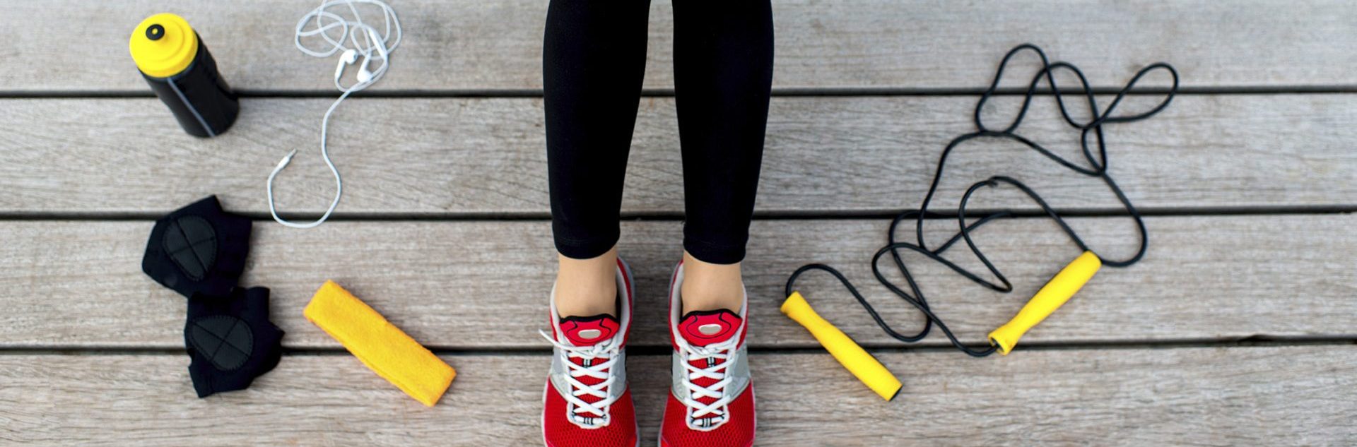 Sporty woman holding phone with empty screen sitting on the sunbed with jump rope, gloves and drink bottle on background