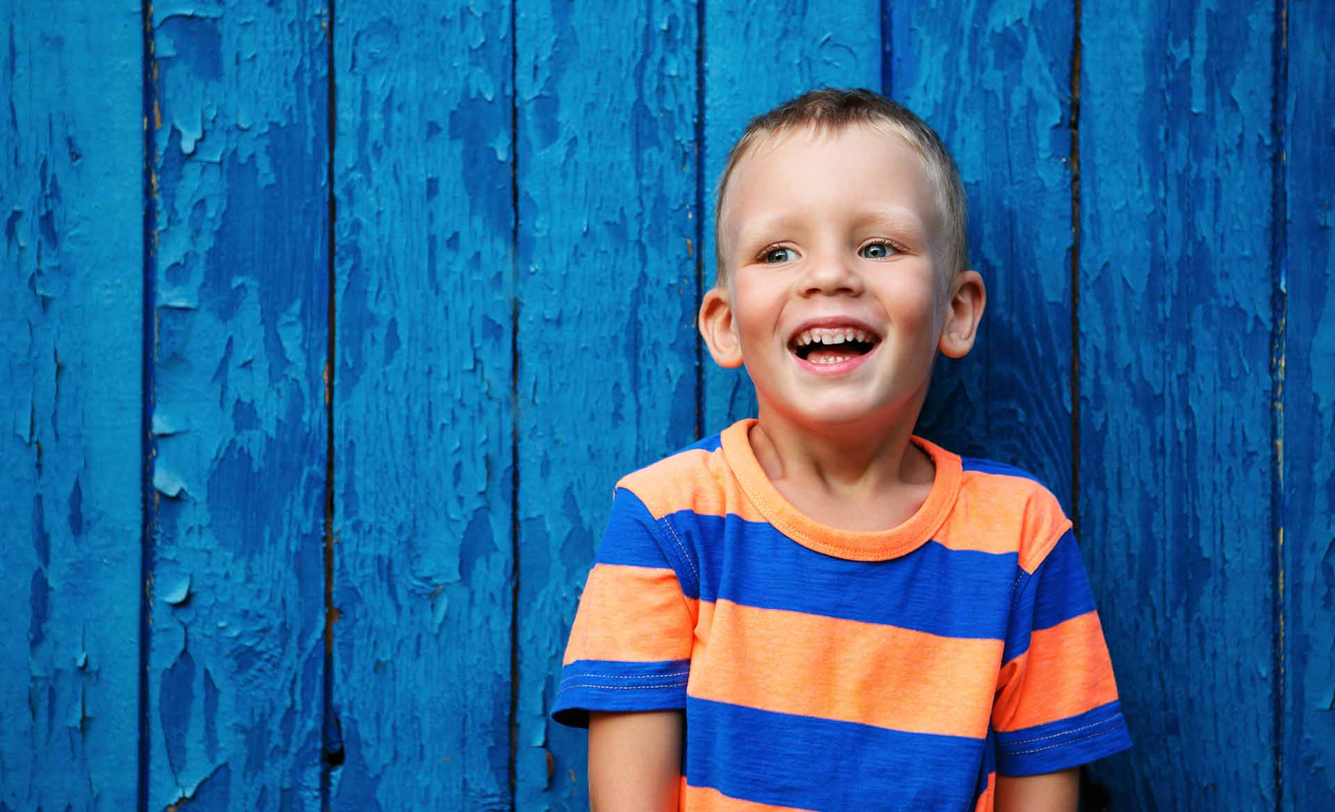 Portrait of happy joyful beautiful little boy against the old textured blue wall