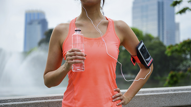 Sweaty woman drinking water during outdoor fitness workout rest. Female runner taking a running break.