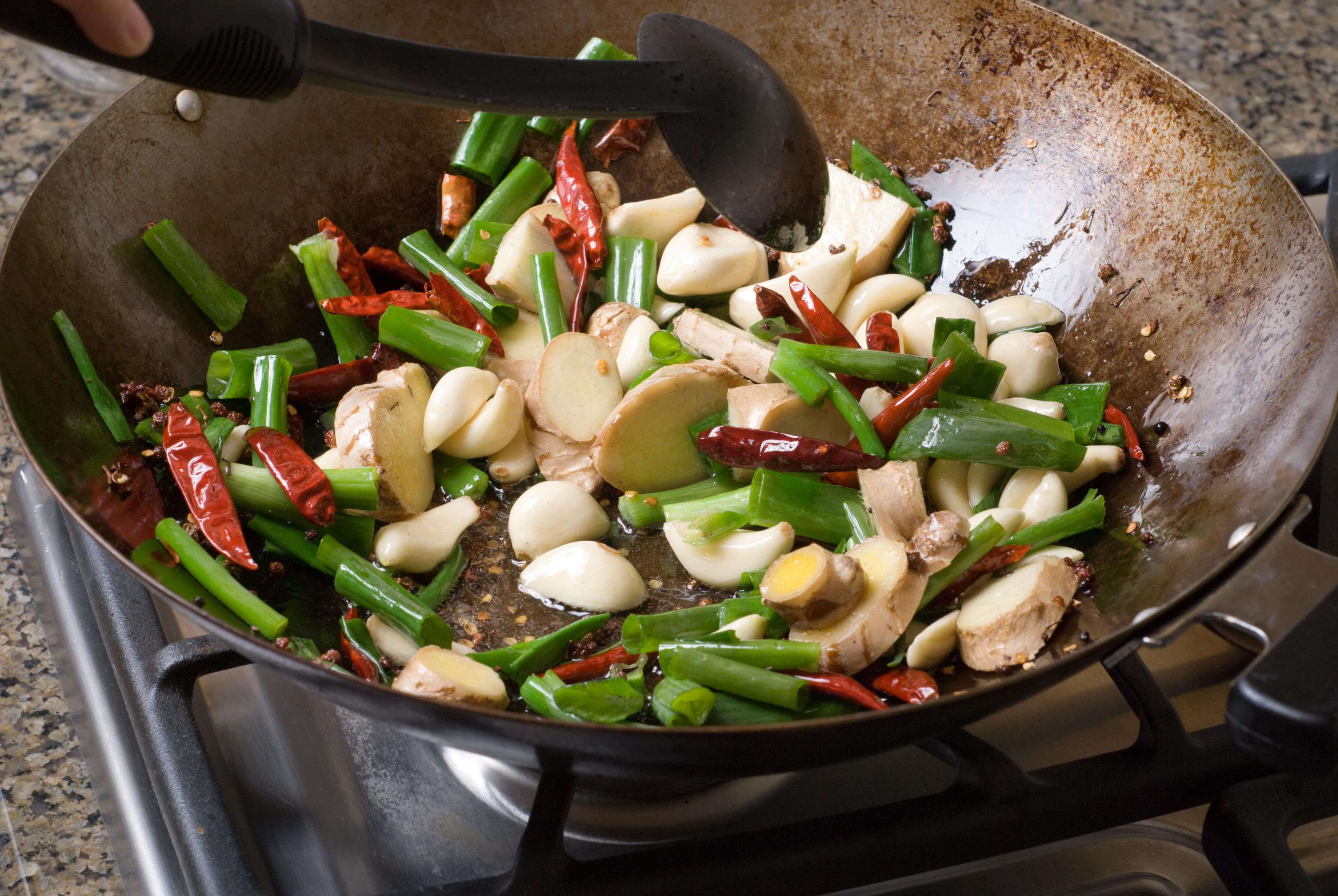 Stir frying chilies, garlic, ginger, green onions and sichuan pepper