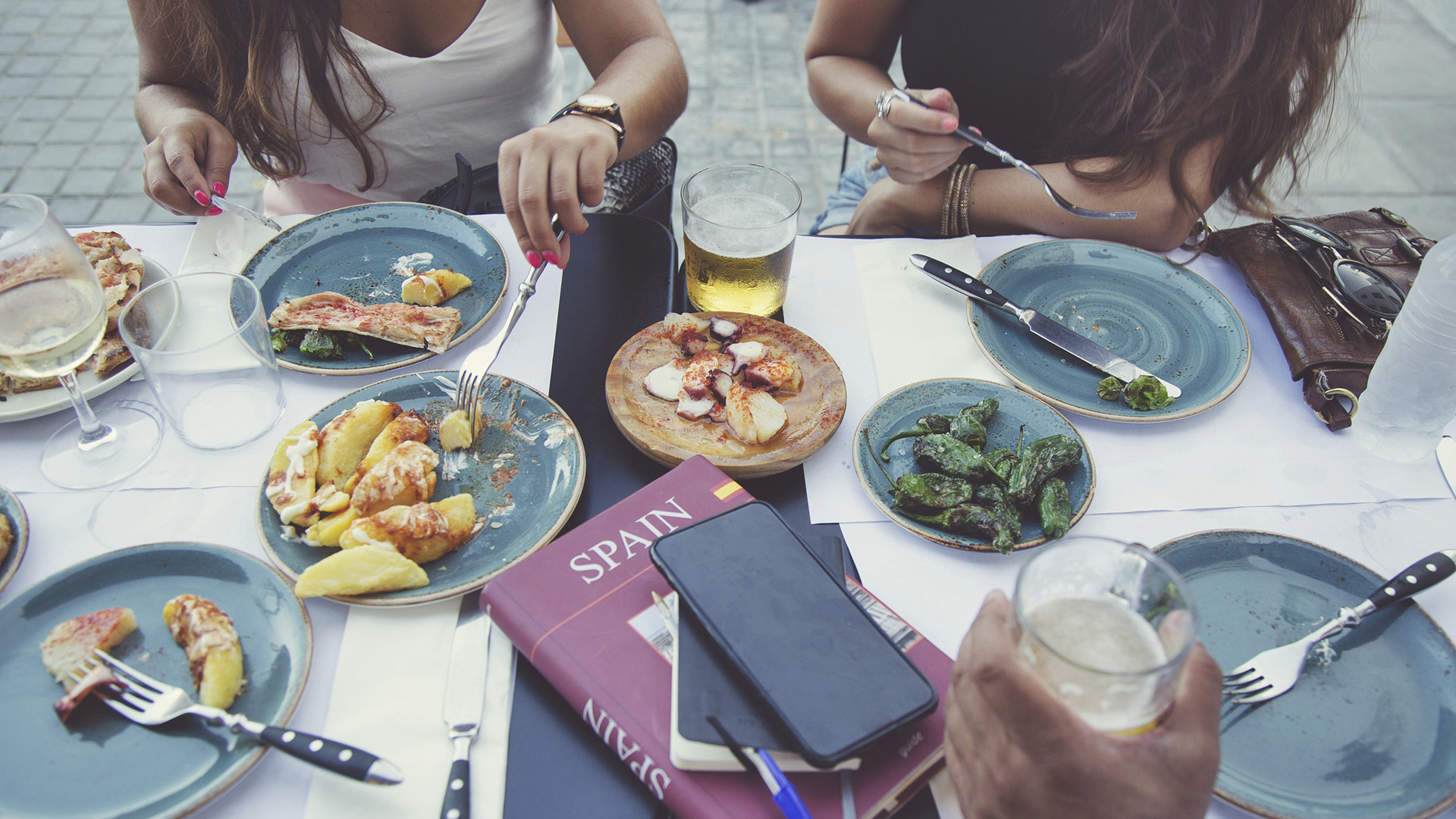 Tourists in Barcelona eating tapas in a typical restaurant in the Barri Gotic. On the table a travel guide of Spain and a smartphone.