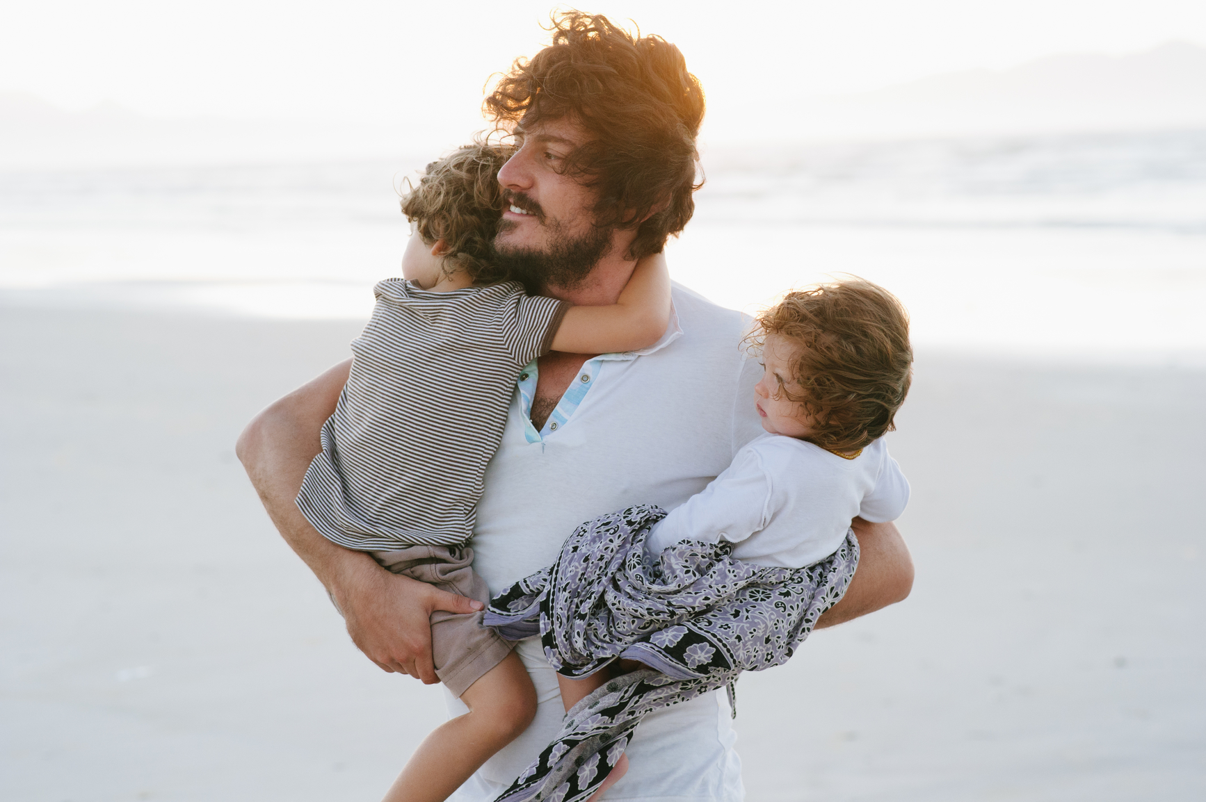 A dad holds his children on the beach at sunrise