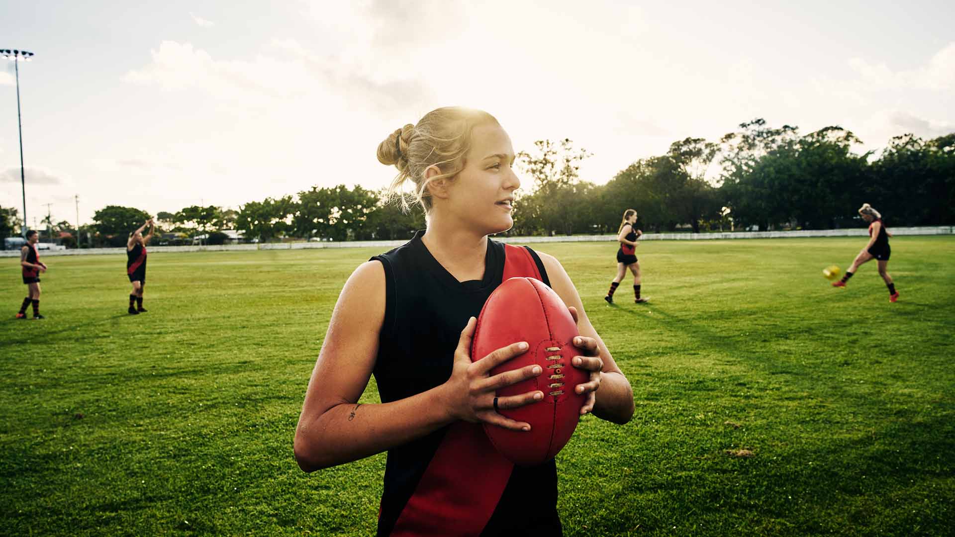 Shot of a young woman holding a football on a field with her team in the background
