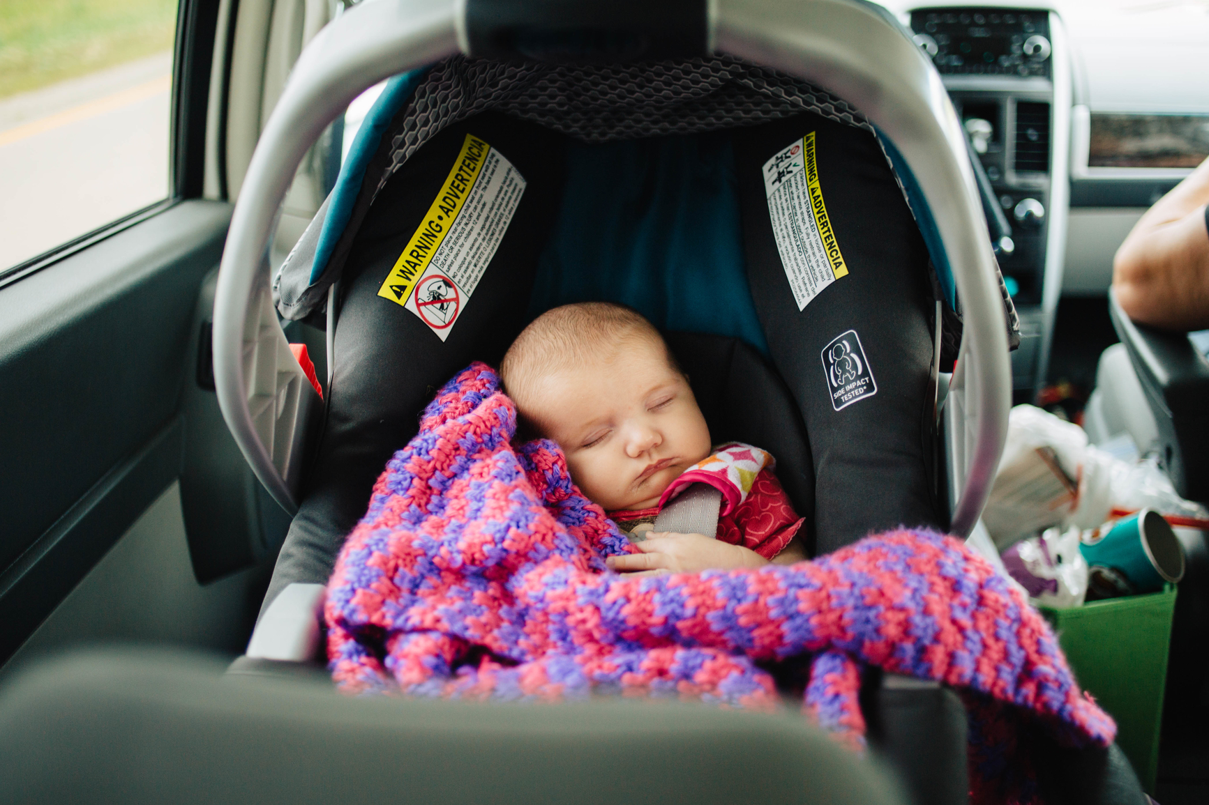 Baby girl sleeping in rear-facing infant seat during a road trip.