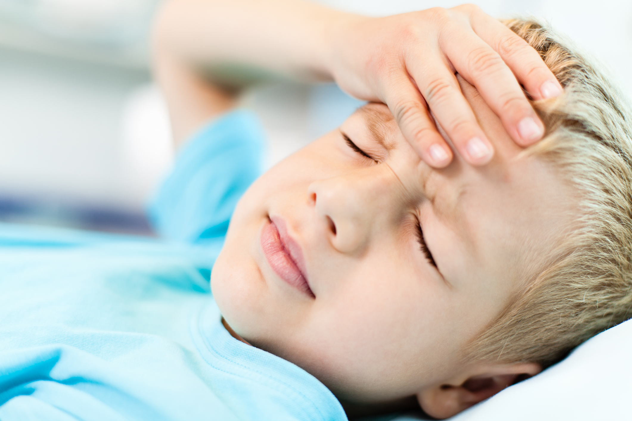 Close-up of little boy with headache, holding his head with his hand.