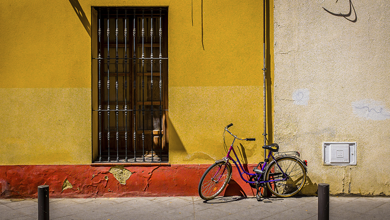 Seville, Spain – May 28, 2015: A Seville street door with metal cage cover and an adjacent parked bicycle on a bright sunny day