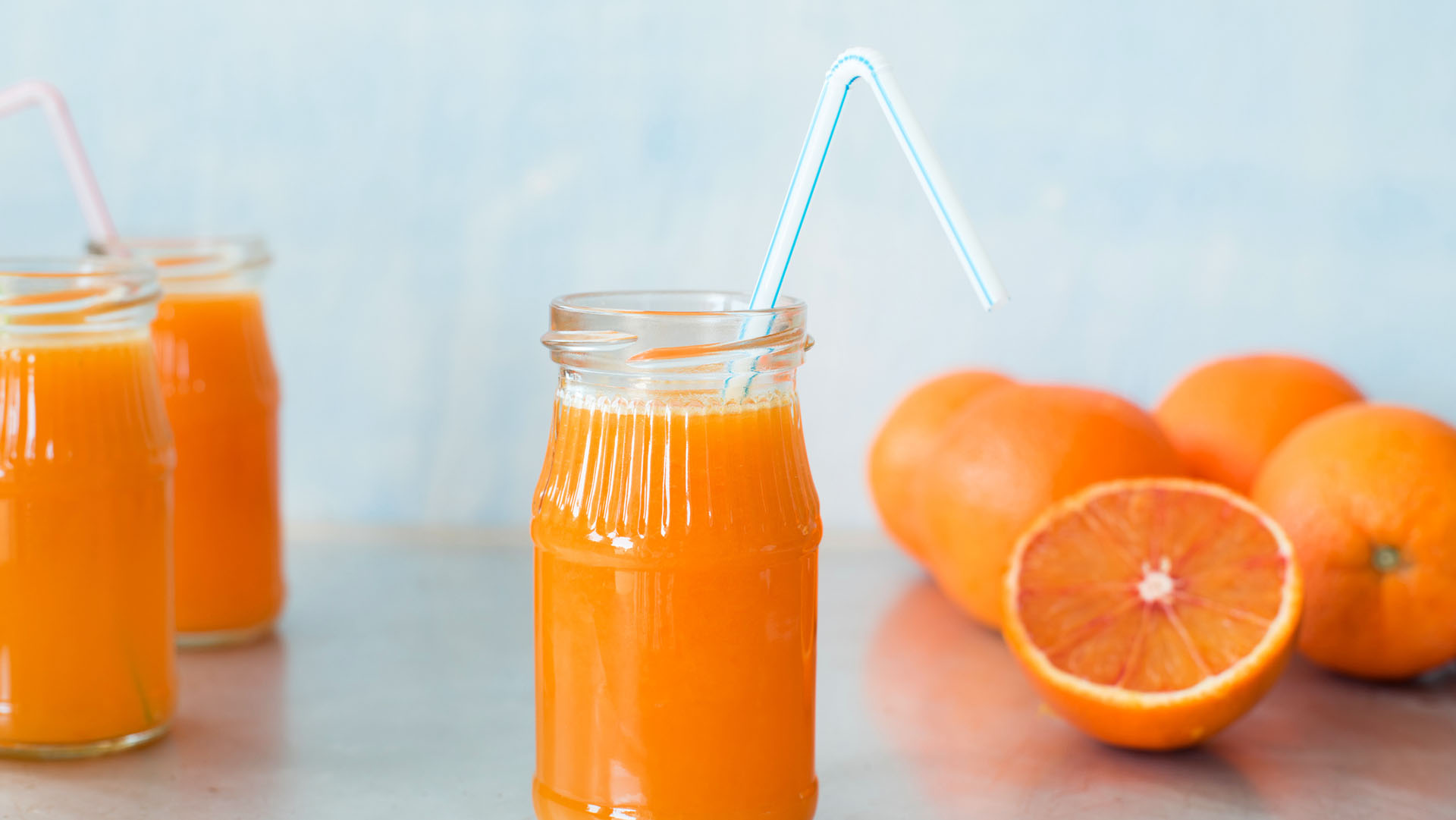 Freshly squeezed orange juice in jar with drinking straw on metallic countertop. Selective focus.