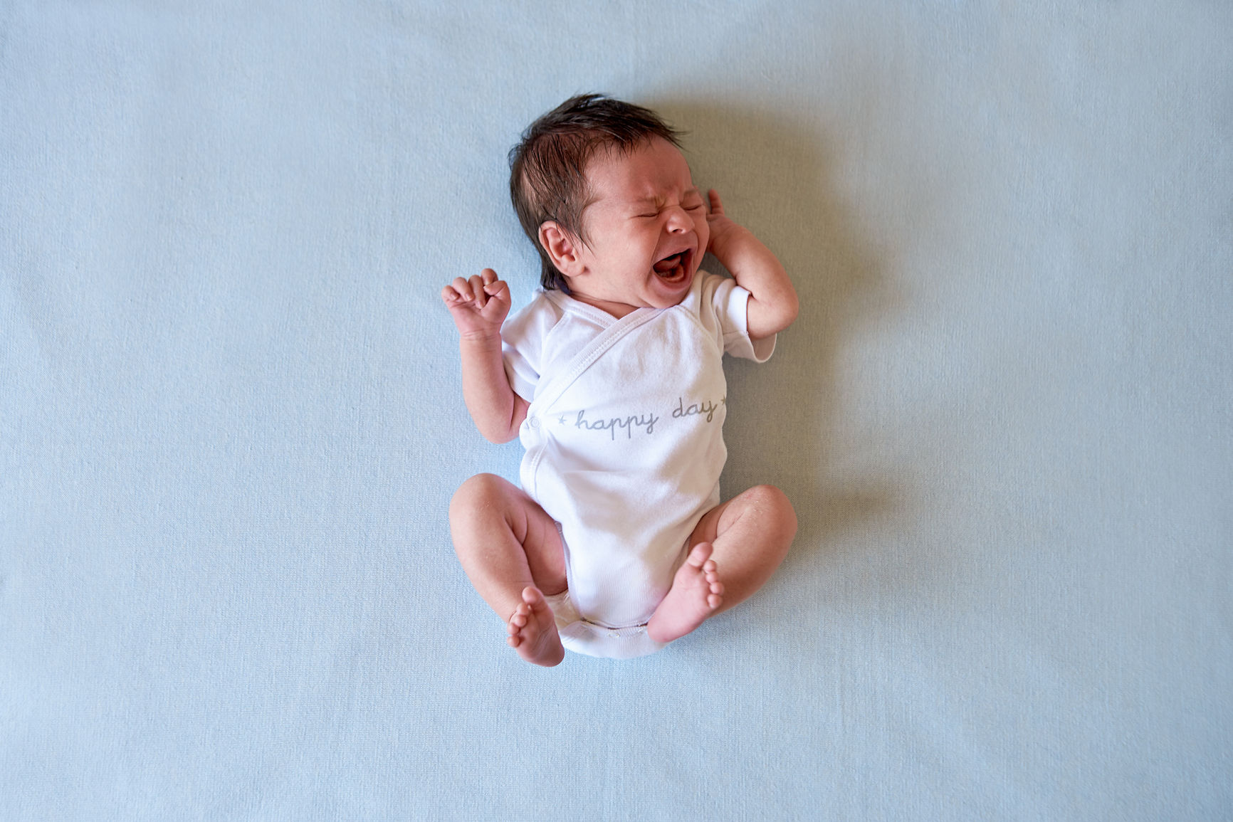 Newborn crying in body with happy day text on white bedcloth.From above
