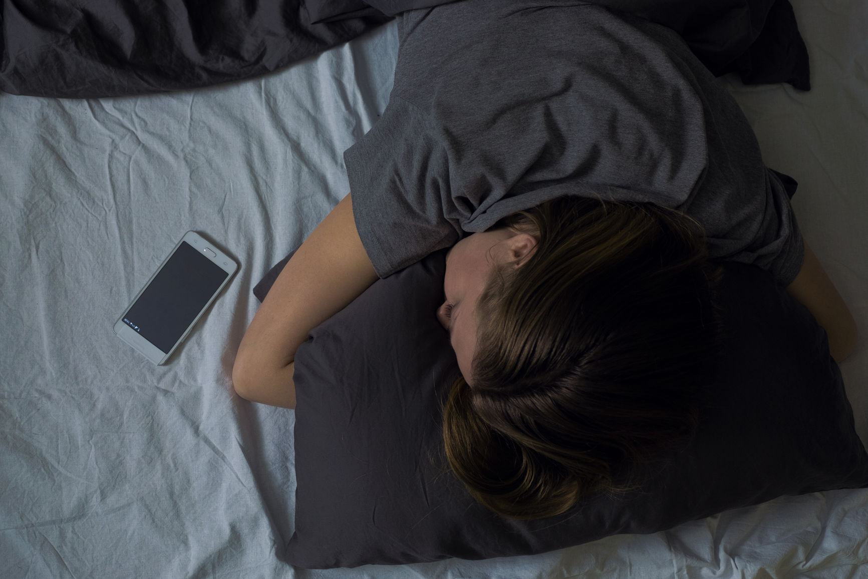 Young woman embracing her pillow and sleeping with enclosed phone. Horizontal indoors shot.