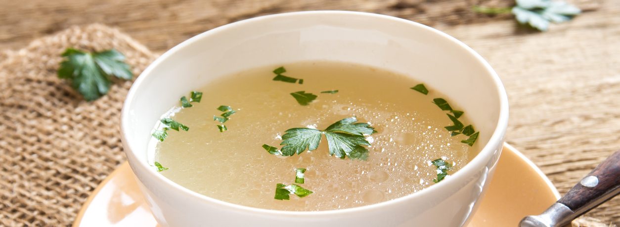 Chicken broth with parsley in white bowl close up