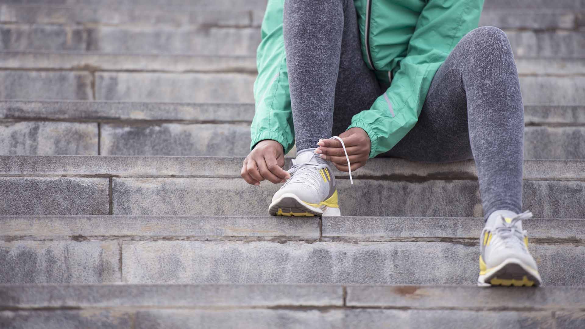 Close up runner female sitting on stairs and tying shoe laces.