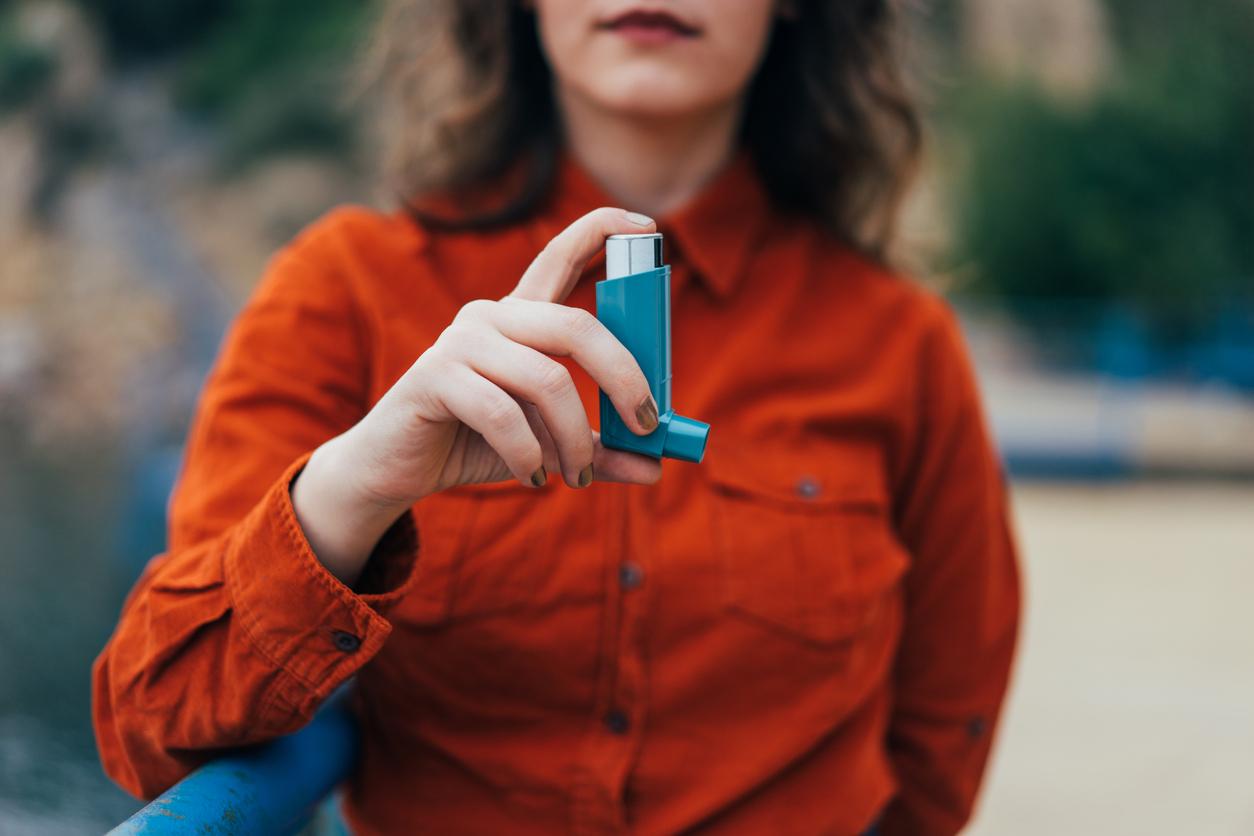 Young woman using an asthma inhaler outdoors