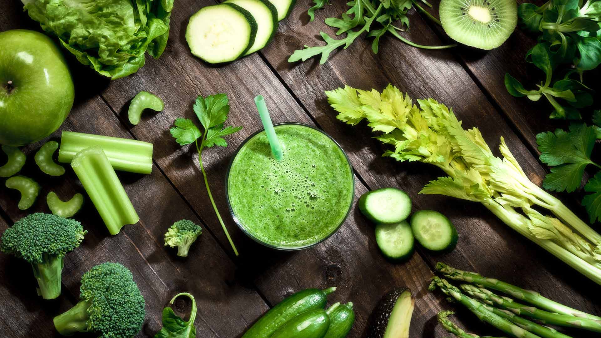 Top view of a rustic wooden table filled with green fruits and vegetables for a perfect detox diet. At the center of the frame is a glass with fresh green smoothie and a large variety of fruits and vegetables are all around it. Soft focus technique used. Low key DSRL studio photo taken with Canon EOS 5D Mk II and Canon EF 100mm f/2.8L Macro IS USM