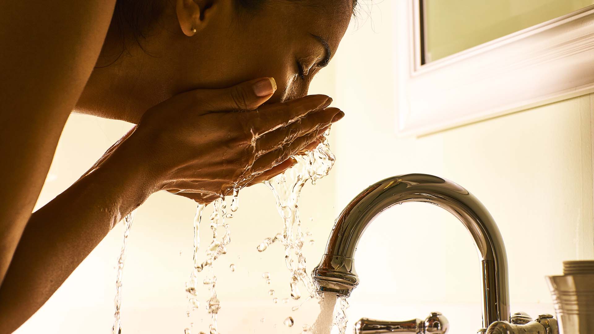 Woman washing face at home using bathroom sink with stainless faucet.