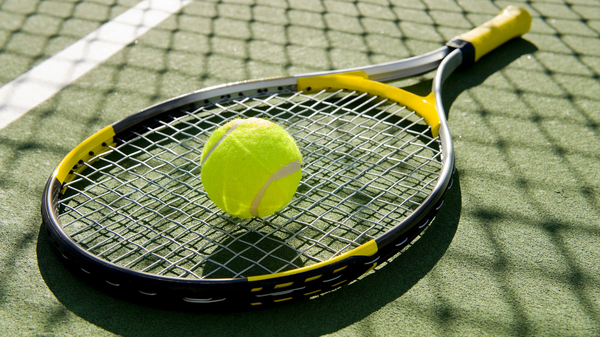 A tennis racket and new tennis ball on a freshly painted tennis court