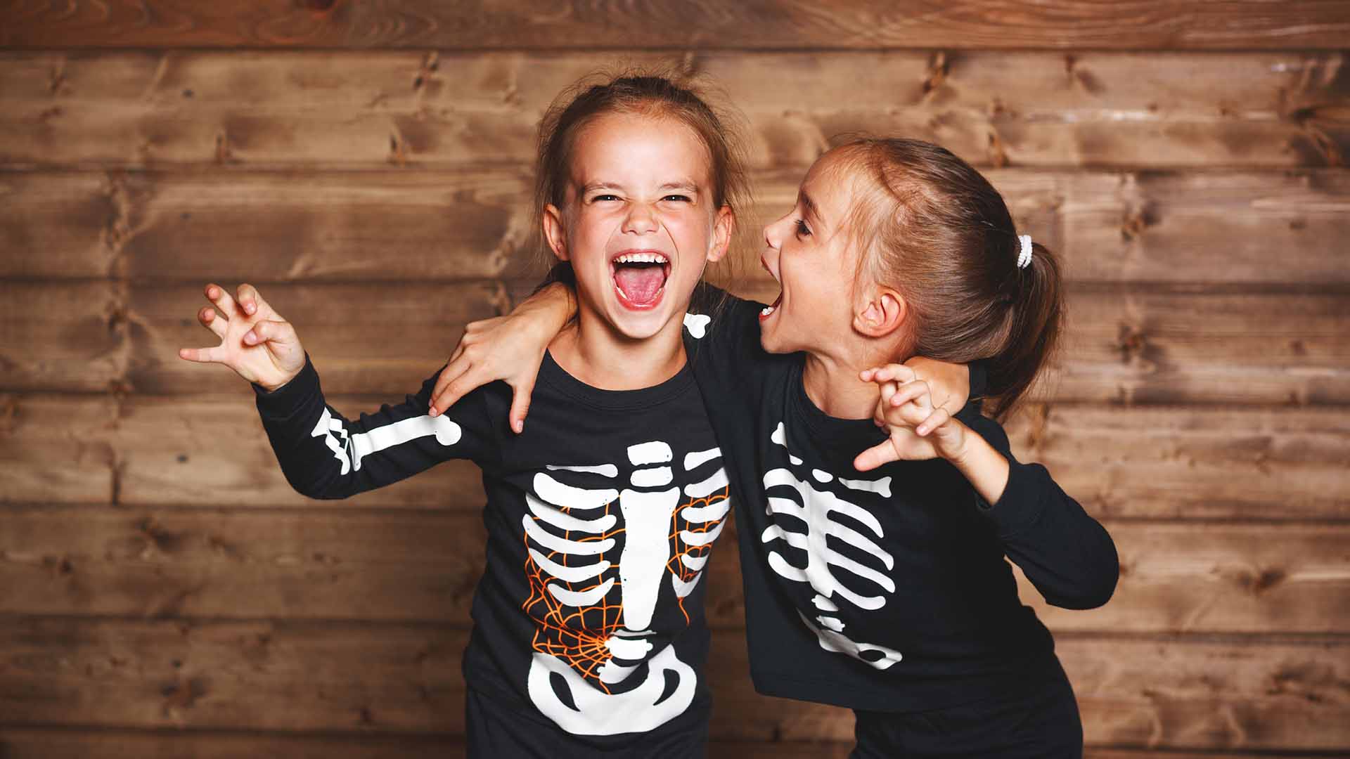 holiday halloween. funny funny sisters twins children in carnival costumes skeleton on a wooden background