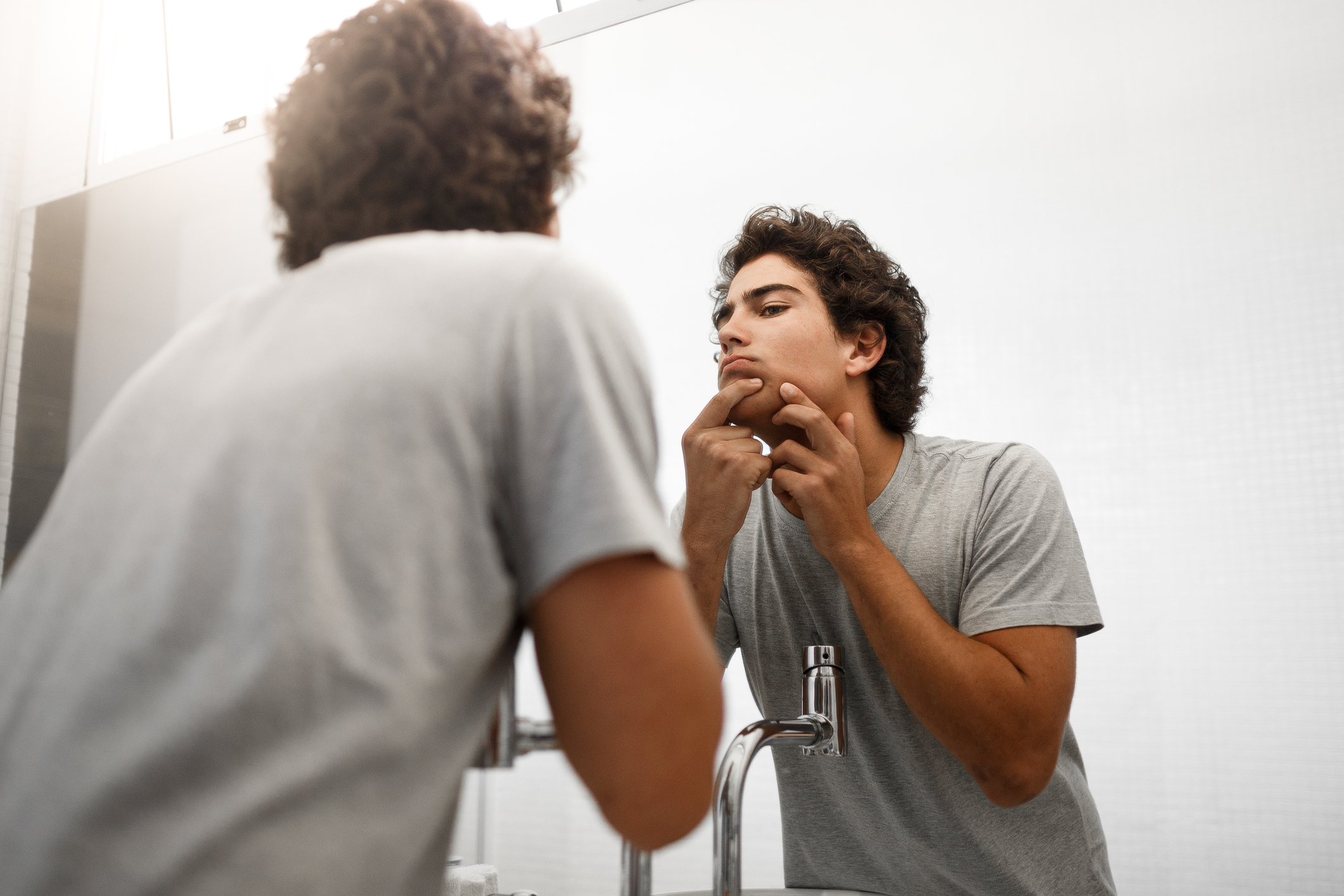 A young boy squeezing pimple in front of bathroom mirror.