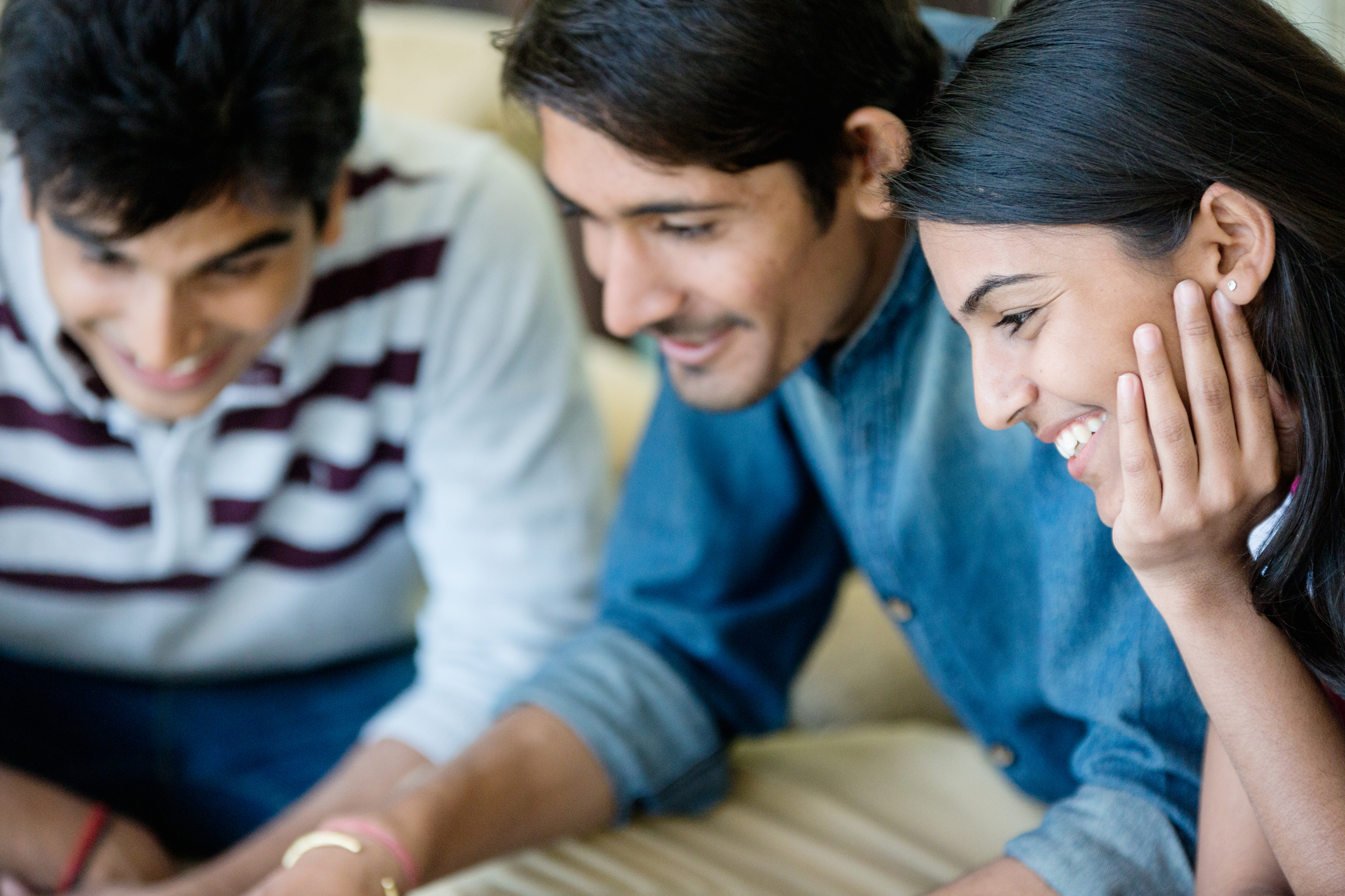 Three young Indian friends enjoying the time they spend together while looking at something on a laptop screen, which is not visible in the image.