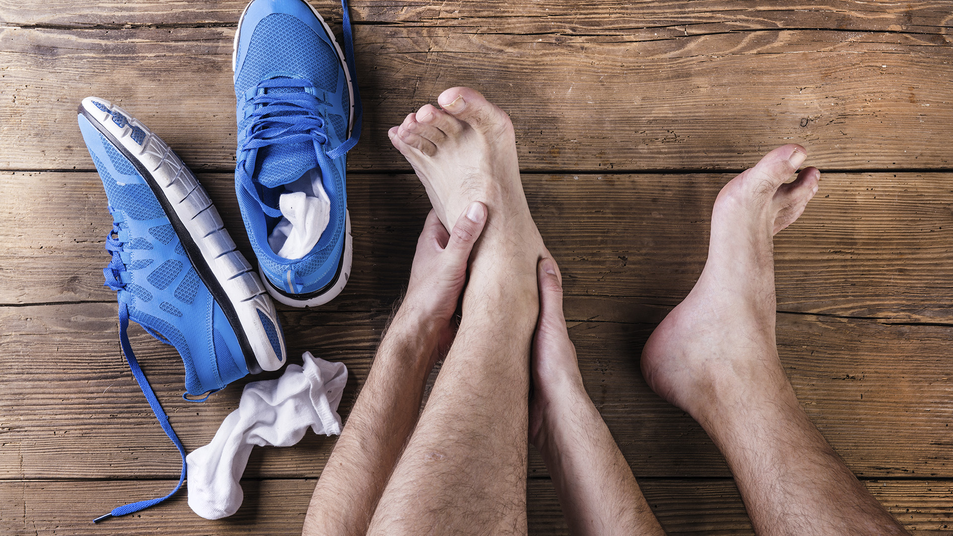 Unrecognizable injured runner sitting on a wooden floor background