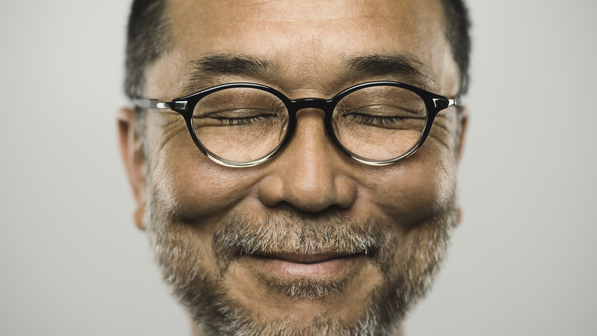 Studio portrait of a japanese mature man looking at camera with relaxed expression. The man has around 50 years and has glasses, short hair and a short grey beard. Vertical colour image from a medium format digital camera.