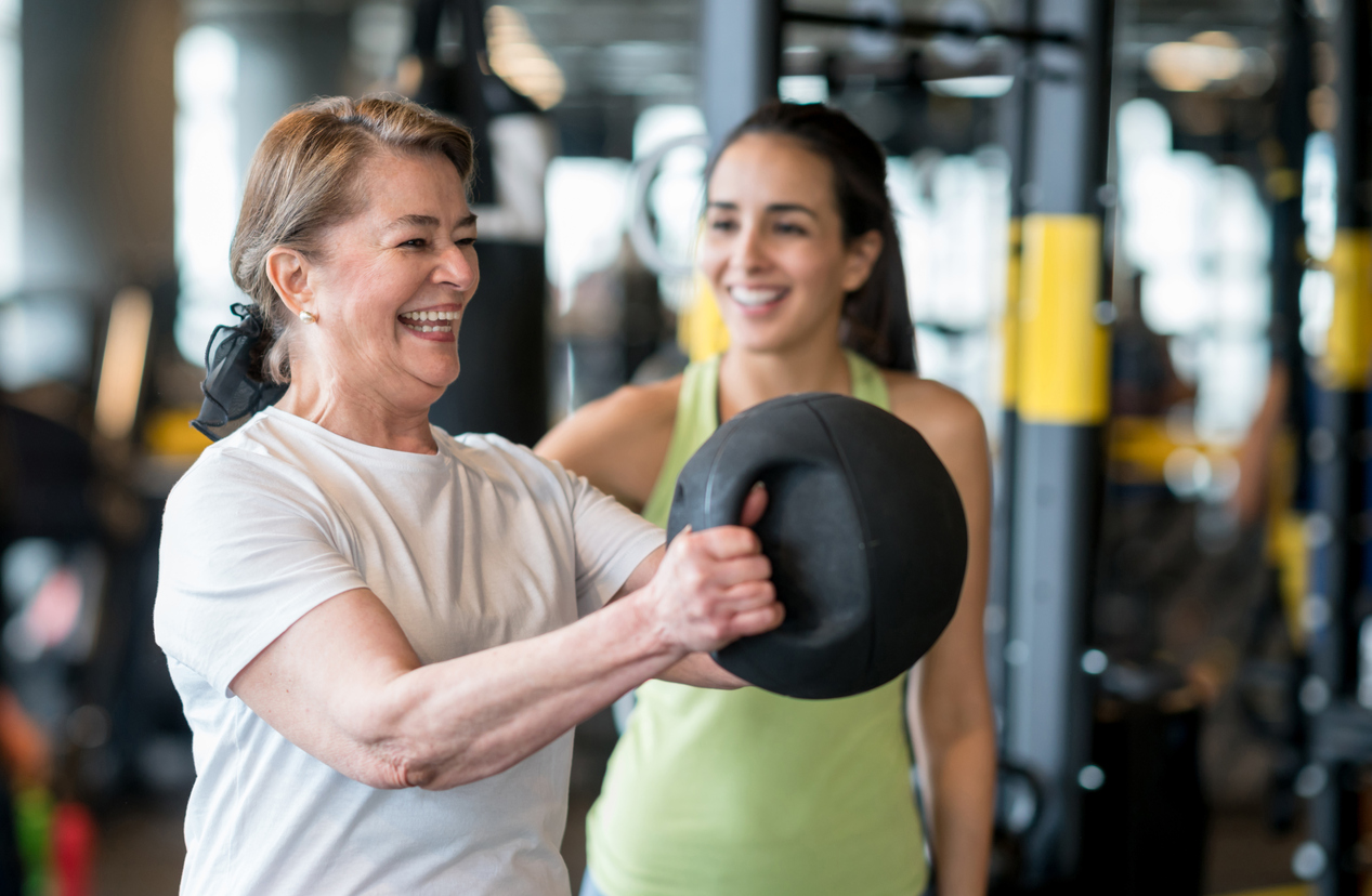 A woman lifts a medicine ball next to a trainer. Strength exercises can ease knee pain and osteoarthritis symptoms. 