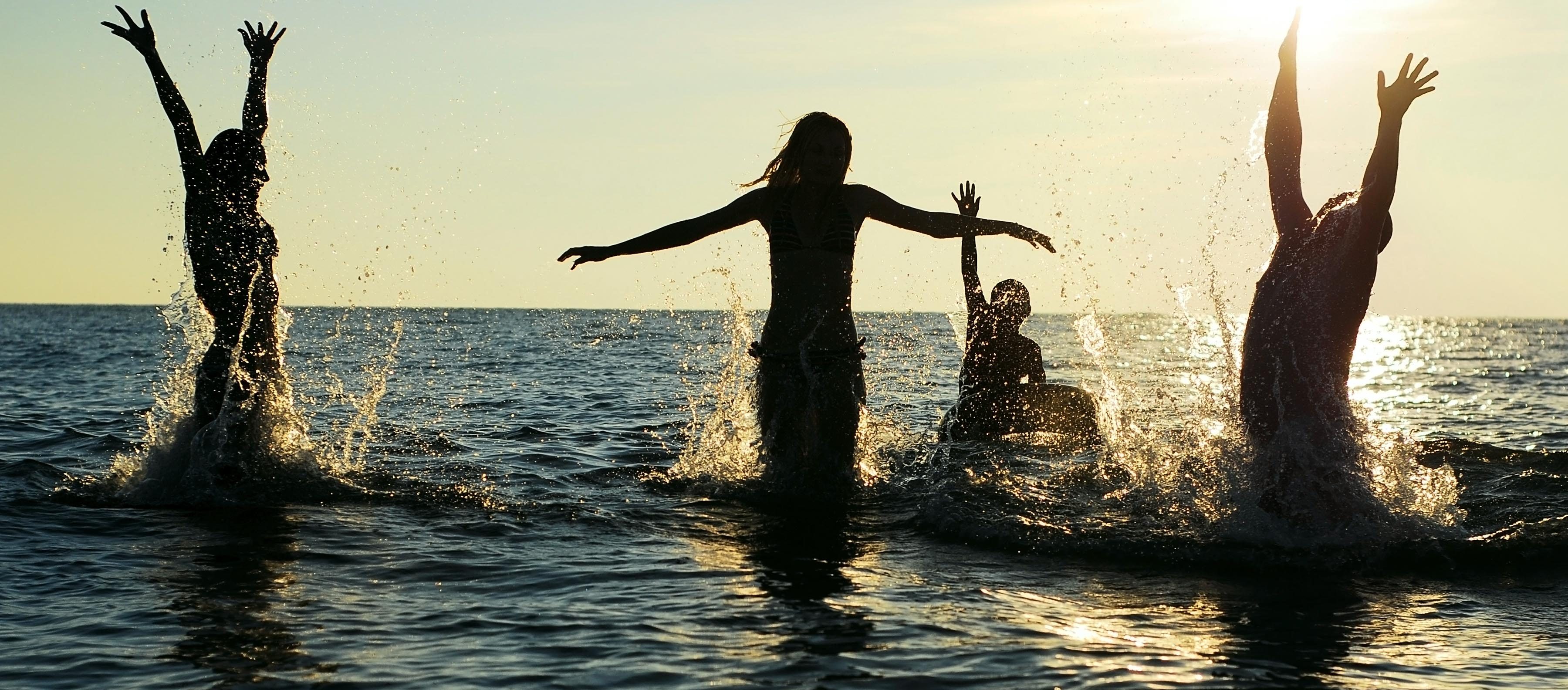 Silhouettes of young group of people jumping in ocean at sunset