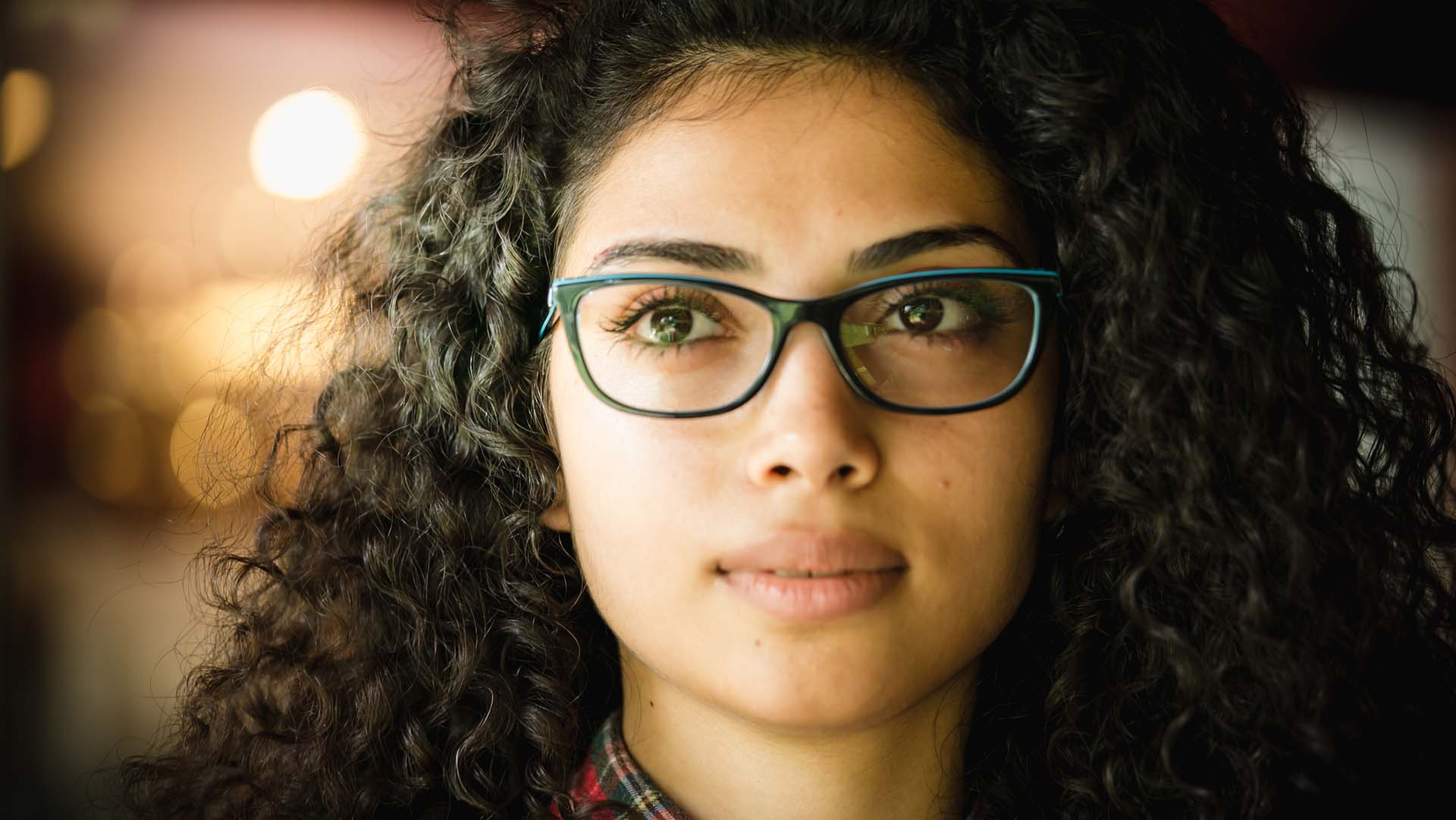 Young woman with curly hair and wearing glasses, looking away from camera.