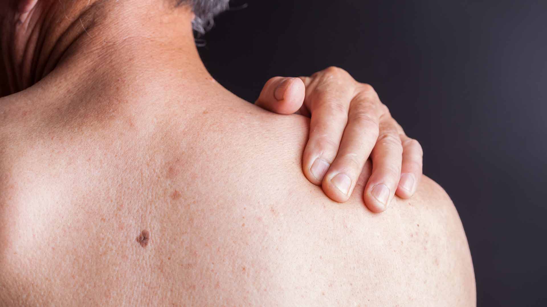 old man holding his shoulder with blackbackground studio shot